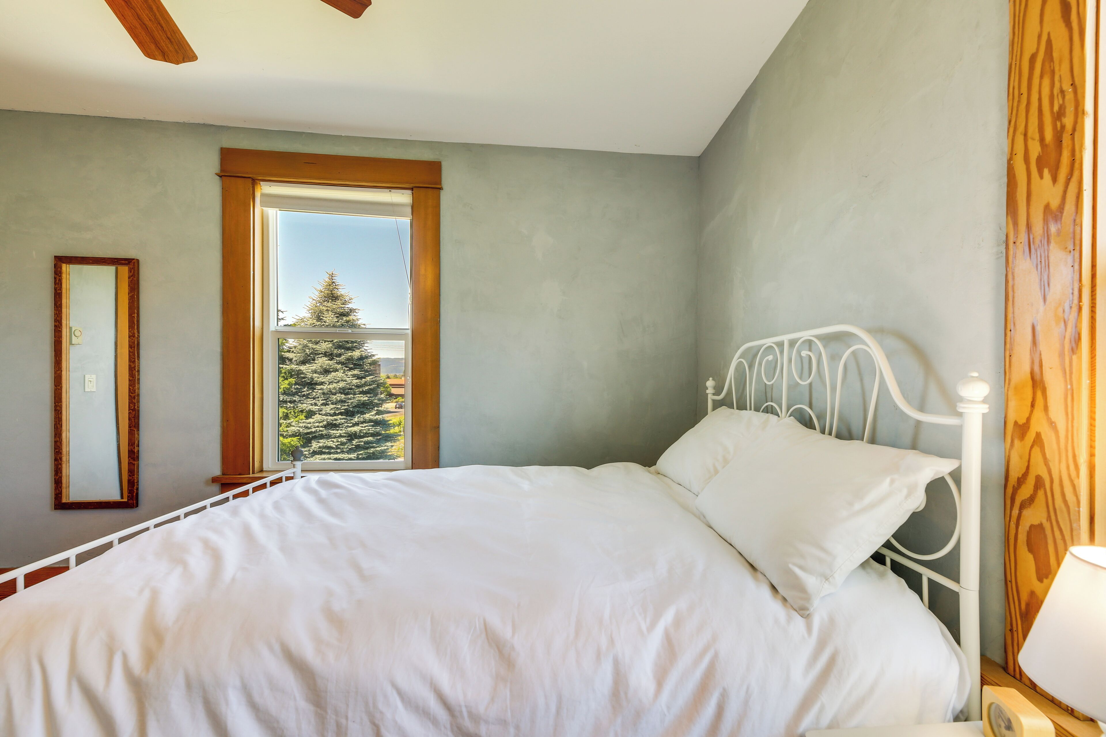 A bedroom with a large bed, a window with a view of a tree, and a wooden headboard.