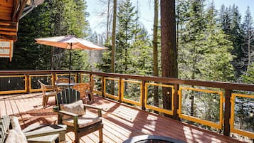 A wooden deck with outdoor furniture, a fire pit, and a view of a forest.