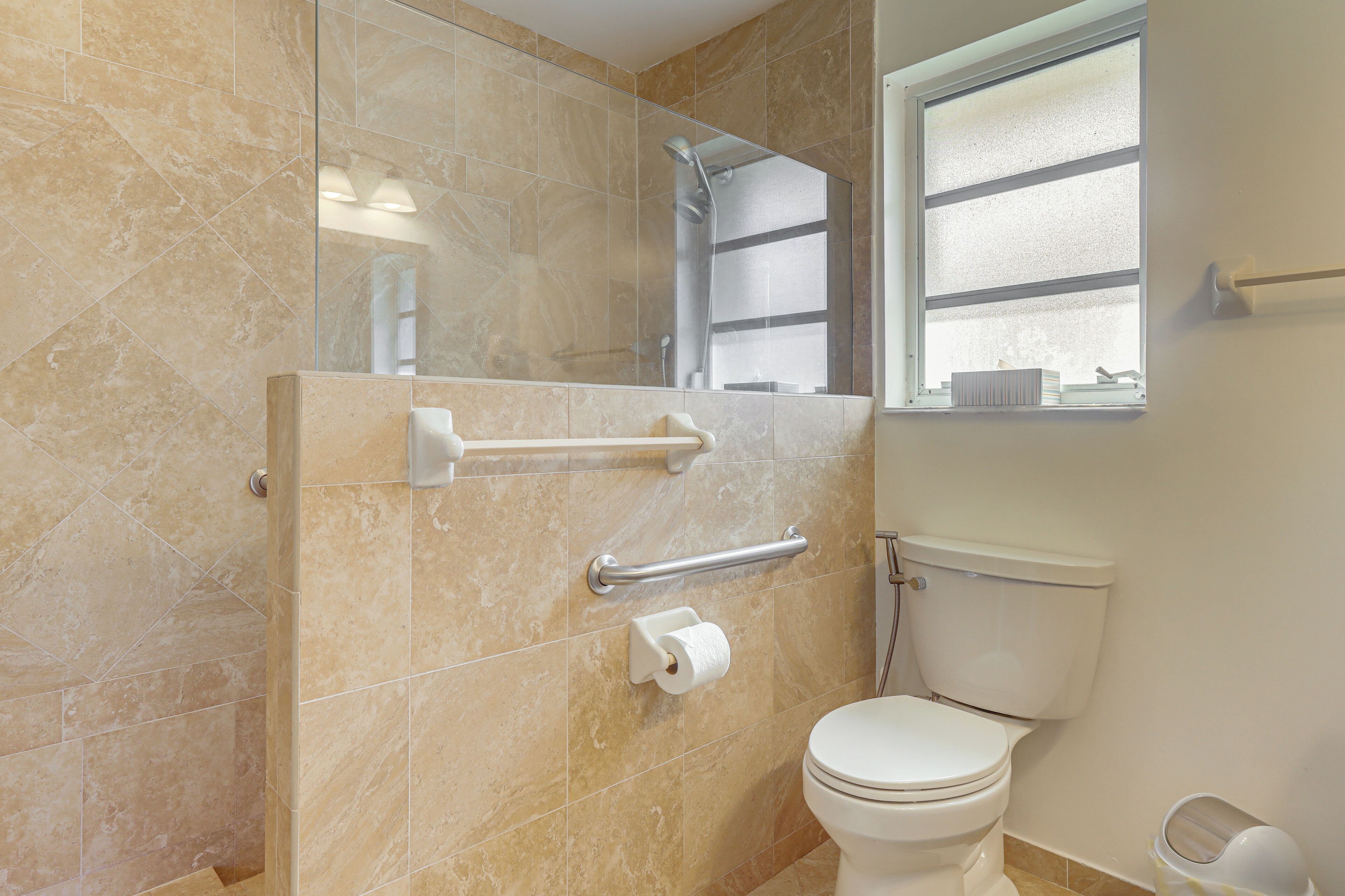 A bathroom with a toilet, a shower, and a handrail.