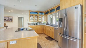 A modern kitchen with wooden cabinets, a stainless steel refrigerator, and a granite countertop. - Riviera Beach Home w/ Pool - Walk to Beaches! (Singer Island)