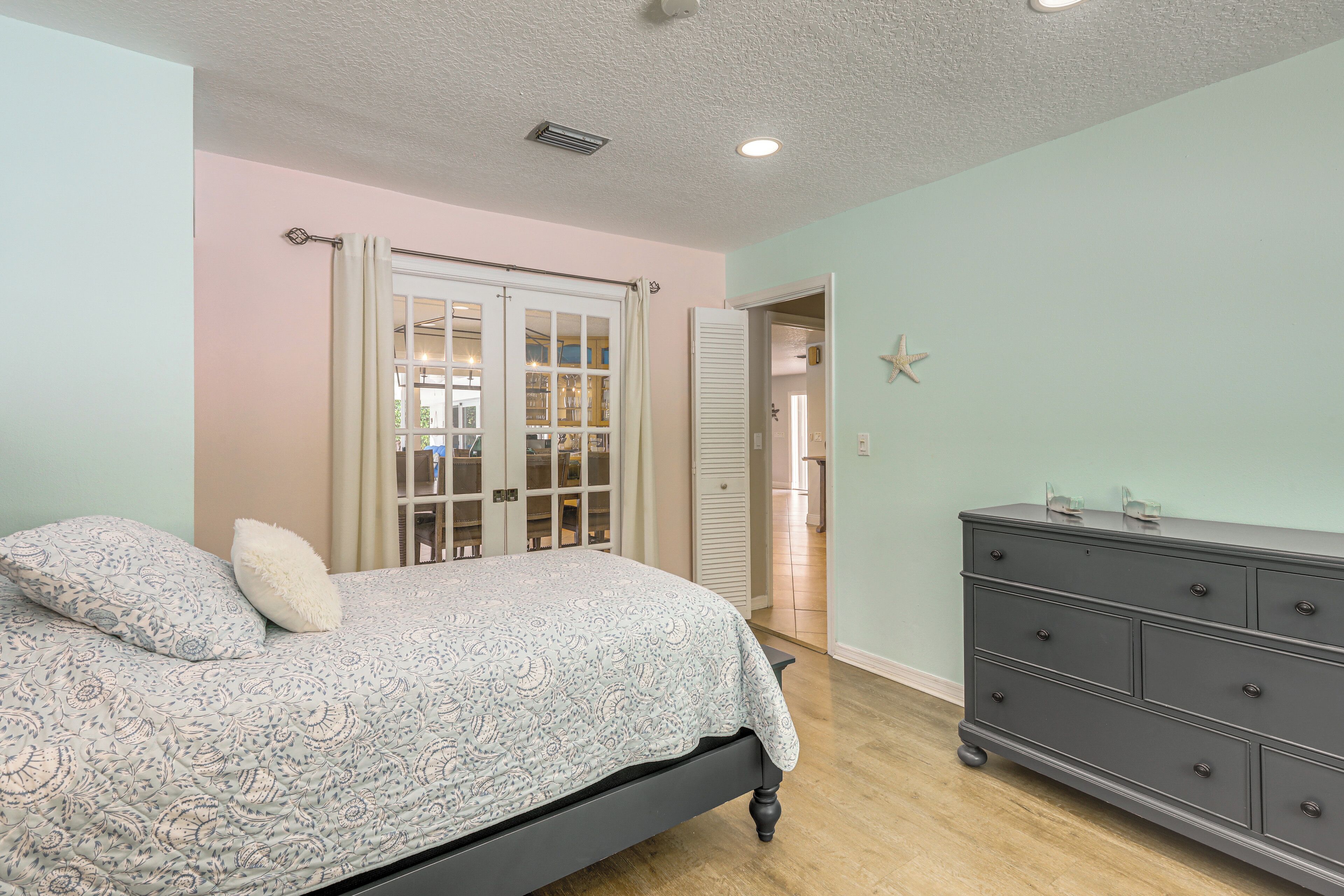 A bedroom with a bed, dresser, and a door leading to another room.