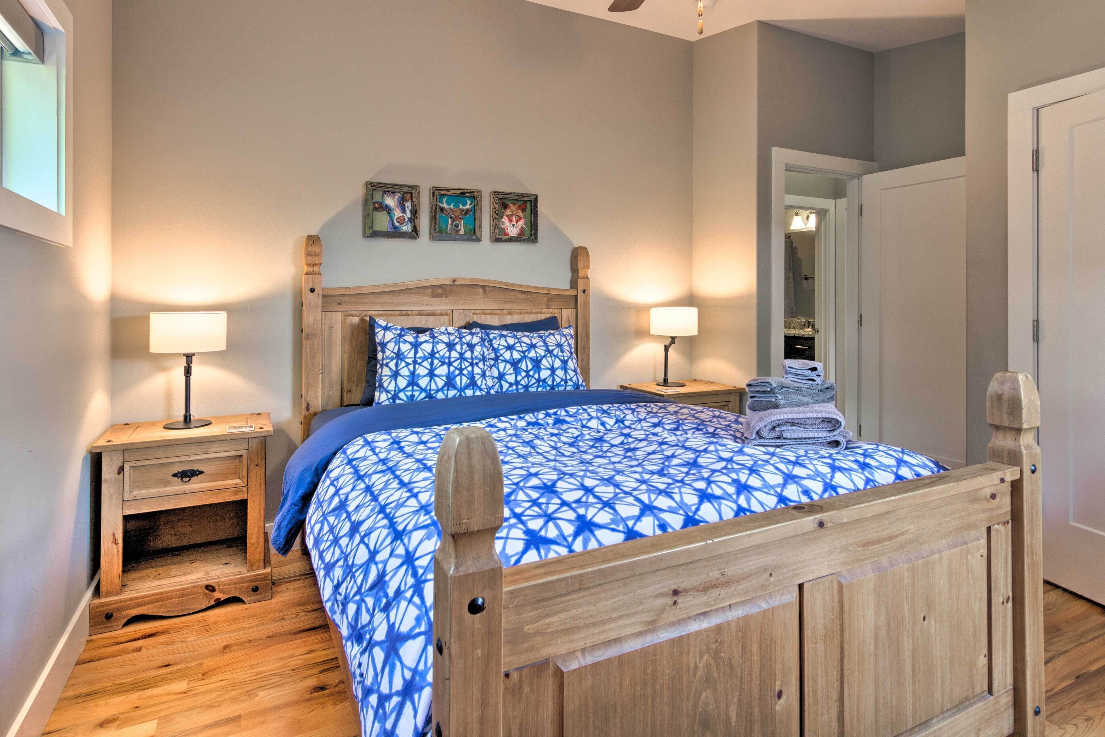 Een slaapkamer met een houten bedframe, een blauw bed met een patroon, twee nachtkastjes met lampen en een deur naar een inloopkast.