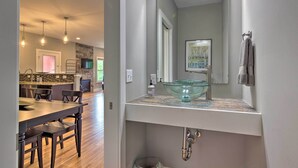 A modern kitchen with a stone backsplash, a dining area with a wooden table and chairs, and a bathroom with a glass bowl sink and a large mirror. - Modern Asheville Greenway Residence w/ 2 Decks! (Asheville)