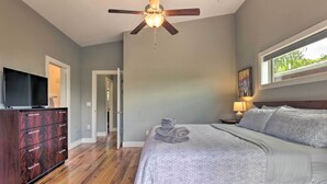 A bedroom with a bed, a ceiling fan, a dresser, a TV, and a window with a view. - Modern Asheville Greenway Residence w/ 2 Decks! (Asheville)