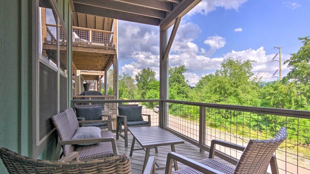 A covered outdoor seating area with wicker furniture and a view of greenery. - Modern Asheville Greenway Residence w/ 2 Decks! (Asheville)