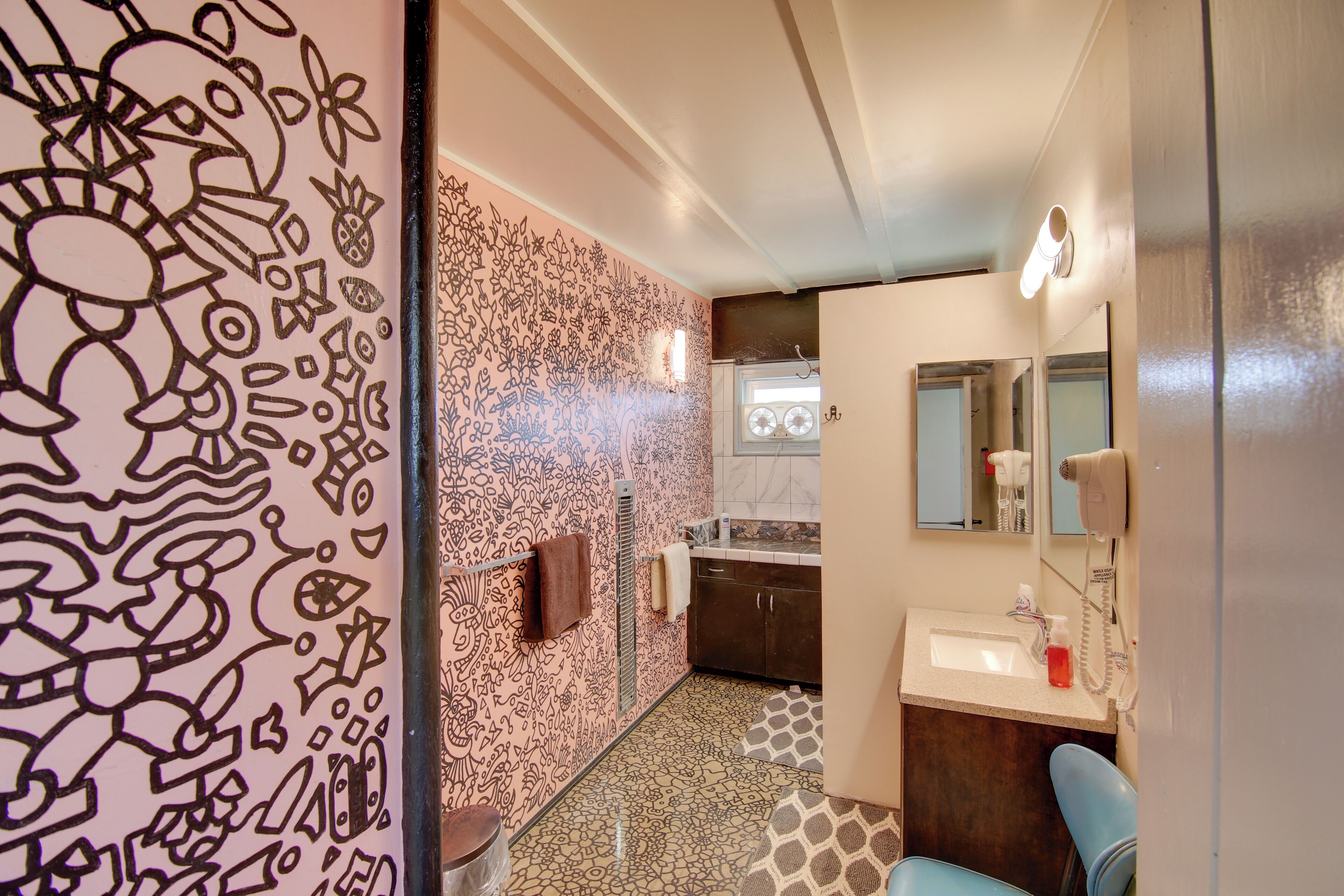 A bathroom with a patterned wall, a sink, a mirror, and a towel rack.