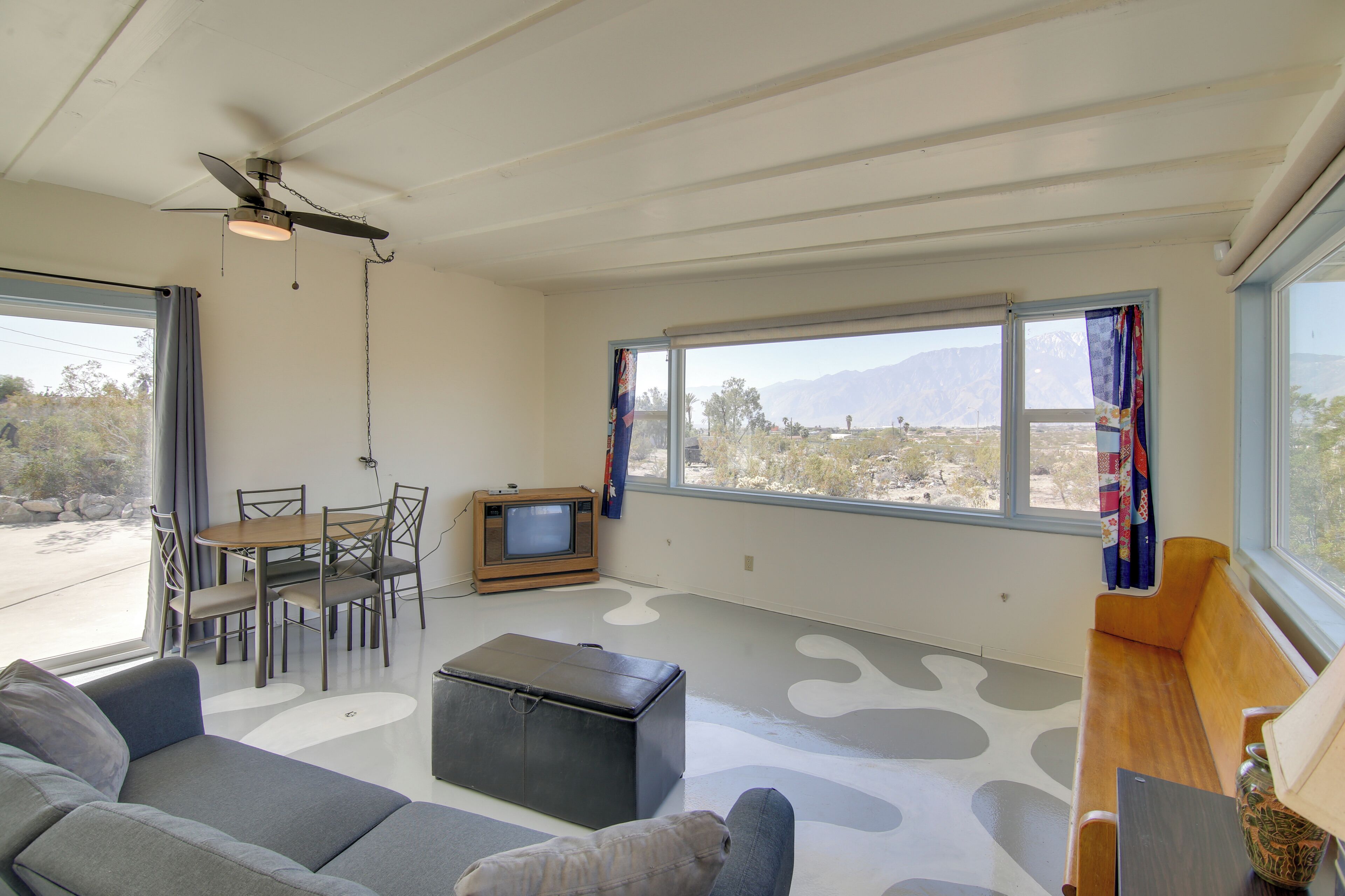 A spacious living area with a sofa, a coffee table, a TV, and a dining table with chairs.