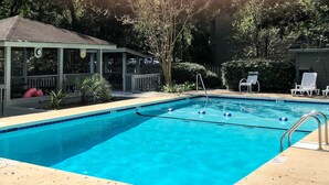 A rectangular swimming pool with clear blue water, surrounded by a concrete deck. There are lounge chairs and a covered seating area with a roof. - Mount Pleasant Condo - Near Charleston & Beaches! (Mount Pleasant)