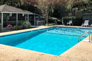 Una piscina rettangolare con acqua cristallina e un bordo in cemento. Sono presenti sedie a sdraio e una zona relax coperta con tetto.