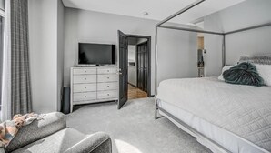 Un dormitorio moderno con cama con dosel, un televisor en una cómoda y un vestidor.