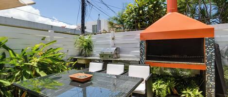 An outdoor patio with a glass table, wicker chairs, a barbecue grill, and a tiled backsplash.