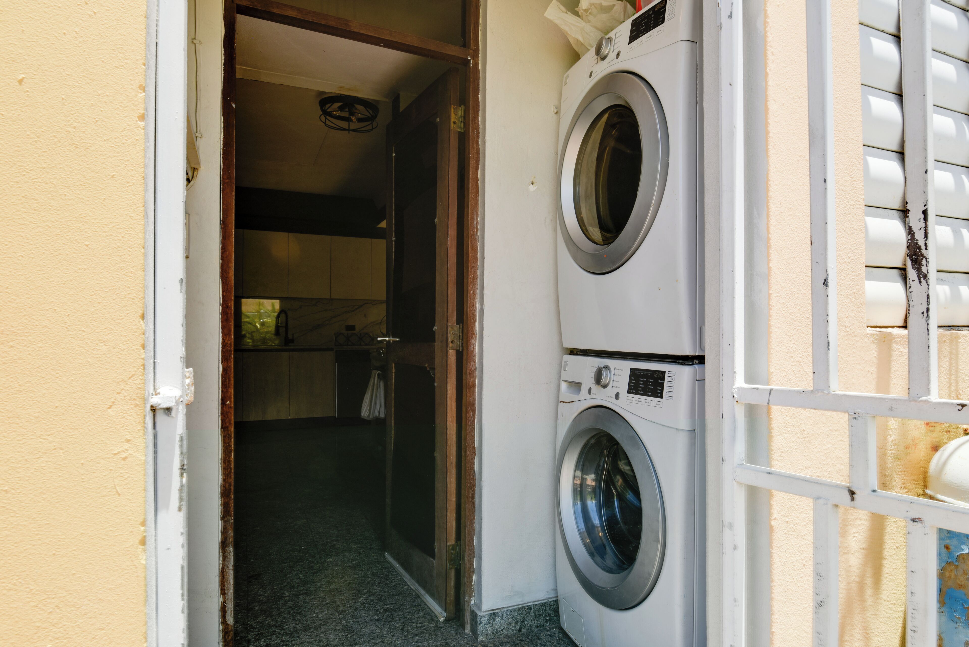 A laundry area with two stacked washing machines, a door leading to another room, and a window with blinds.