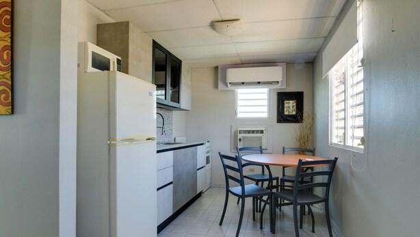 A compact kitchen with a refrigerator, microwave, and stove, a dining table with chairs, and a window with blinds. - Walk to Isla Verde Beach! Home w/ Heated Pool (Carolina)