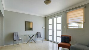 Un salón amplio con una mesa de vidrio, dos sillas, un sofá y un amplio ventanal corredero.