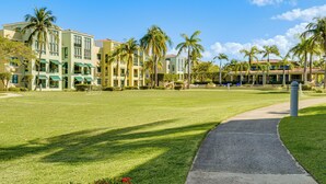 A hotel with a grassy lawn, palm trees, and a pathway leading to the entrance. - Aquatika Resort Condo w/ Private Beach Access! (Loiza)