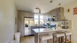 A modern kitchen with a large island, wooden cabinets, stainless steel appliances, and a window providing natural light. - Aquatika Resort Condo w/ Private Beach Access! (Loiza)