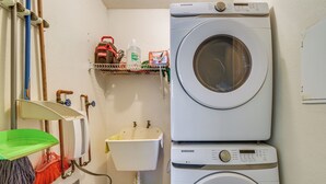 A laundry area with two stacked washing machines, a shelf with cleaning supplies, and a mop rack. - Aquatika Resort Condo w/ Private Beach Access! (Loiza)