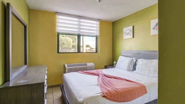 A bedroom with a bed, a nightstand, a mirror, a window with blinds, and a wall-mounted air conditioner. - Aquatika Resort Condo w/ Private Beach Access! (Loiza)