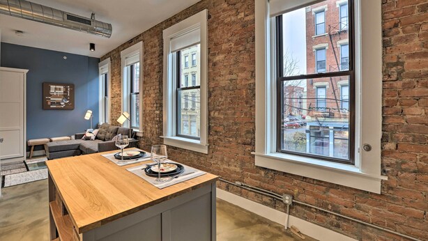 A modern kitchen with a wooden island, large windows, and a brick wall. - Sleek Studio Near Dtwn Dining & Entertainment (Cincinnati)