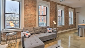 A modern living room with a sectional sofa, large windows, and a brick wall. - Sleek Studio Near Dtwn Dining & Entertainment (Cincinnati)