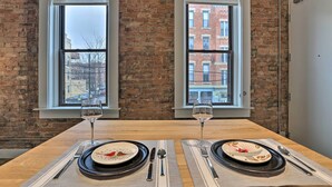 A dining table with two sets of tableware and wine glasses, set against a brick wall with windows overlooking a cityscape. - Sleek Studio Near Dtwn Dining & Entertainment (Cincinnati)