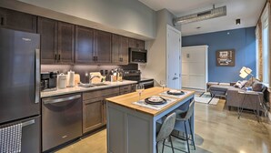 A modern kitchen with dark wooden cabinets, a stainless steel refrigerator, and a wooden island with bar stools. - Sleek Studio Near Dtwn Dining & Entertainment (Cincinnati)
