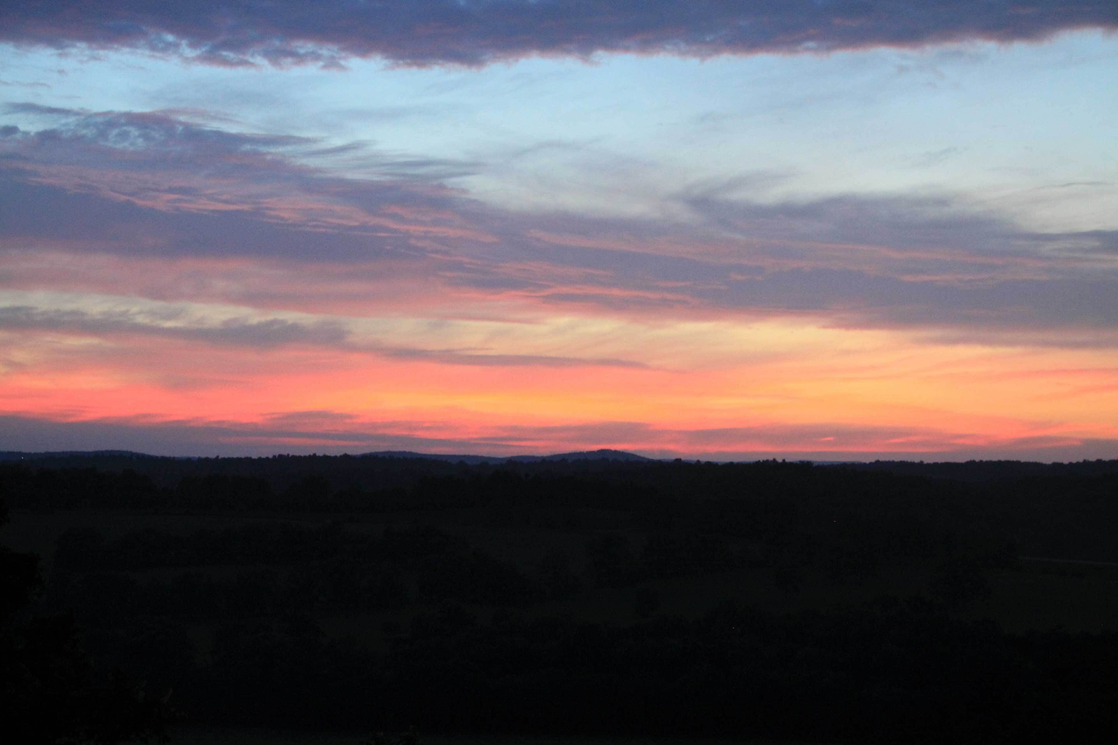 A sunset over a hilly landscape with a clear sky.