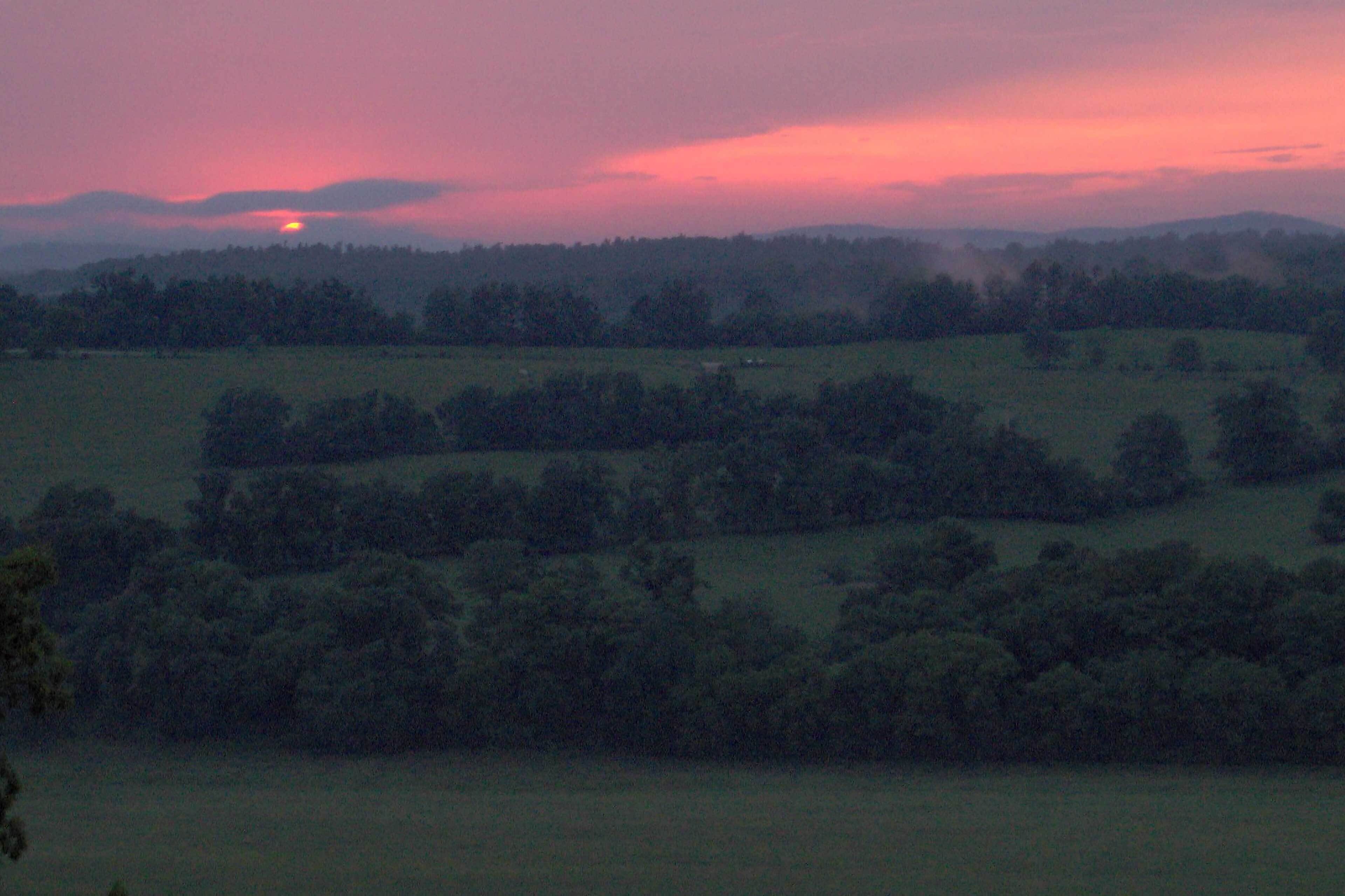 A rural landscape with rolling hills and a sunset.