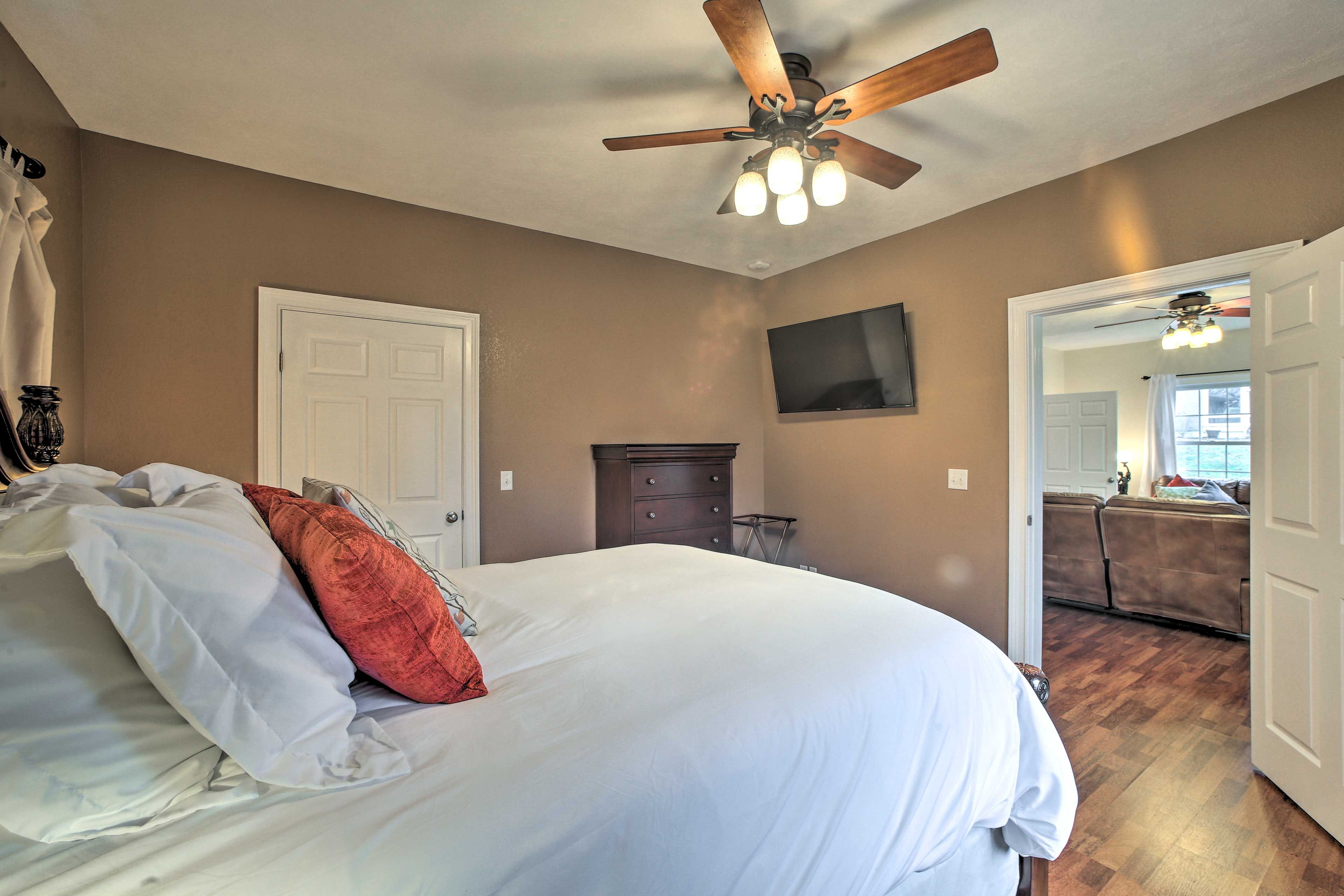 A bedroom with a large bed, a ceiling fan, a dresser, and a TV on the wall.