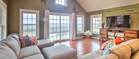 A spacious living room with a large sectional sofa, a flat-screen TV, and a view through large windows.
