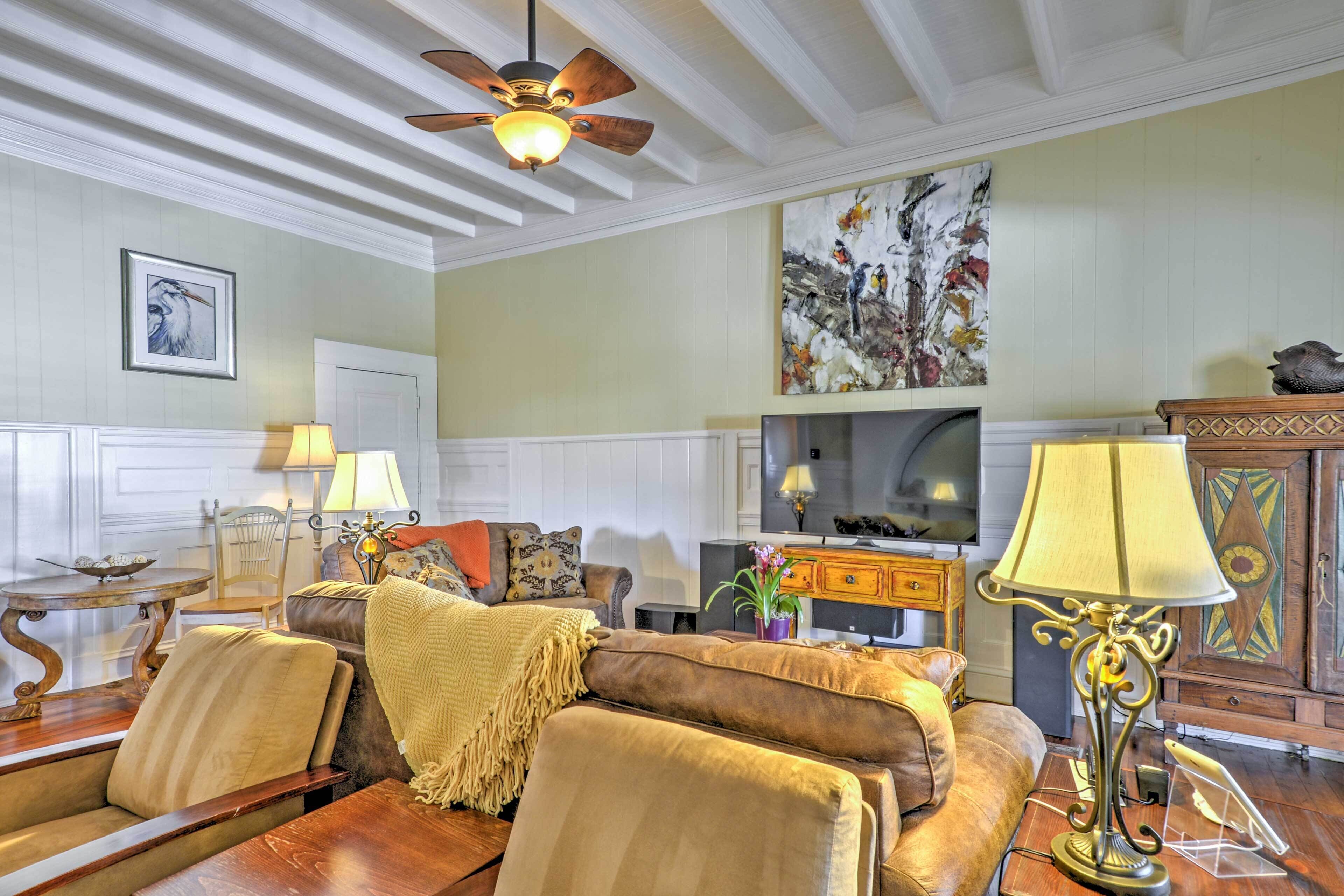 A well-furnished living room with a sofa, chairs, a wooden coffee table, a decorative lamp, and a ceiling fan.
