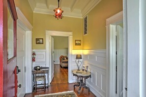 A hallway with a wooden floor, white wainscoting, a red door, a table with a lamp, and a chair. - Carpinteria Apt w/ Hot Tub - 10 Min Walk to Beach! (Carpinteria)