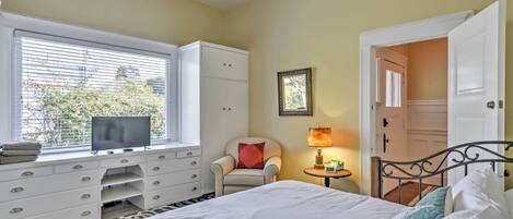 Quarto com uma cama, televisão em uma cômoda, cadeira, abajur e armário.