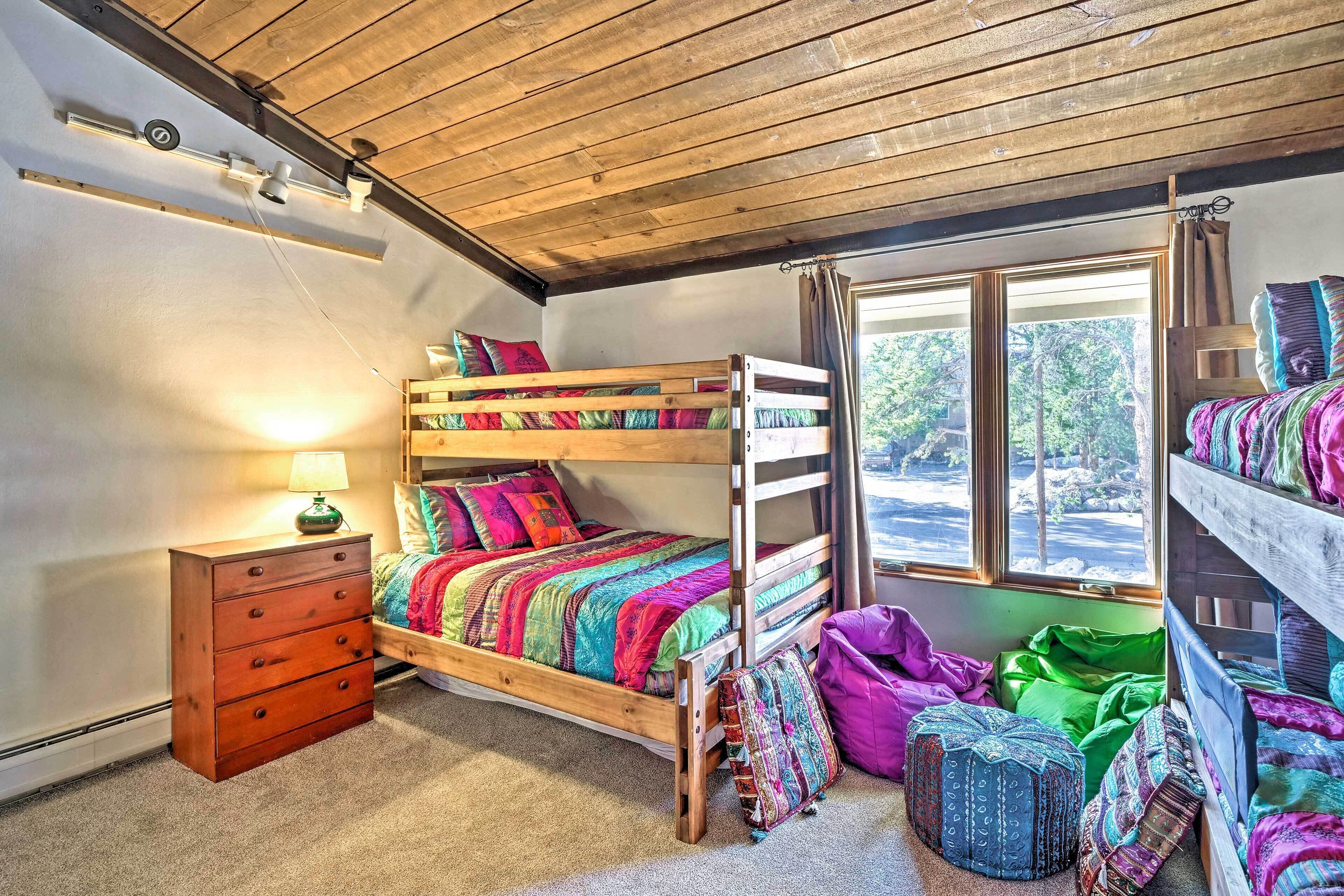 Habitación con literas, techo de madera, ventana con cortinas, cómoda de madera y ropa de cama colorida.