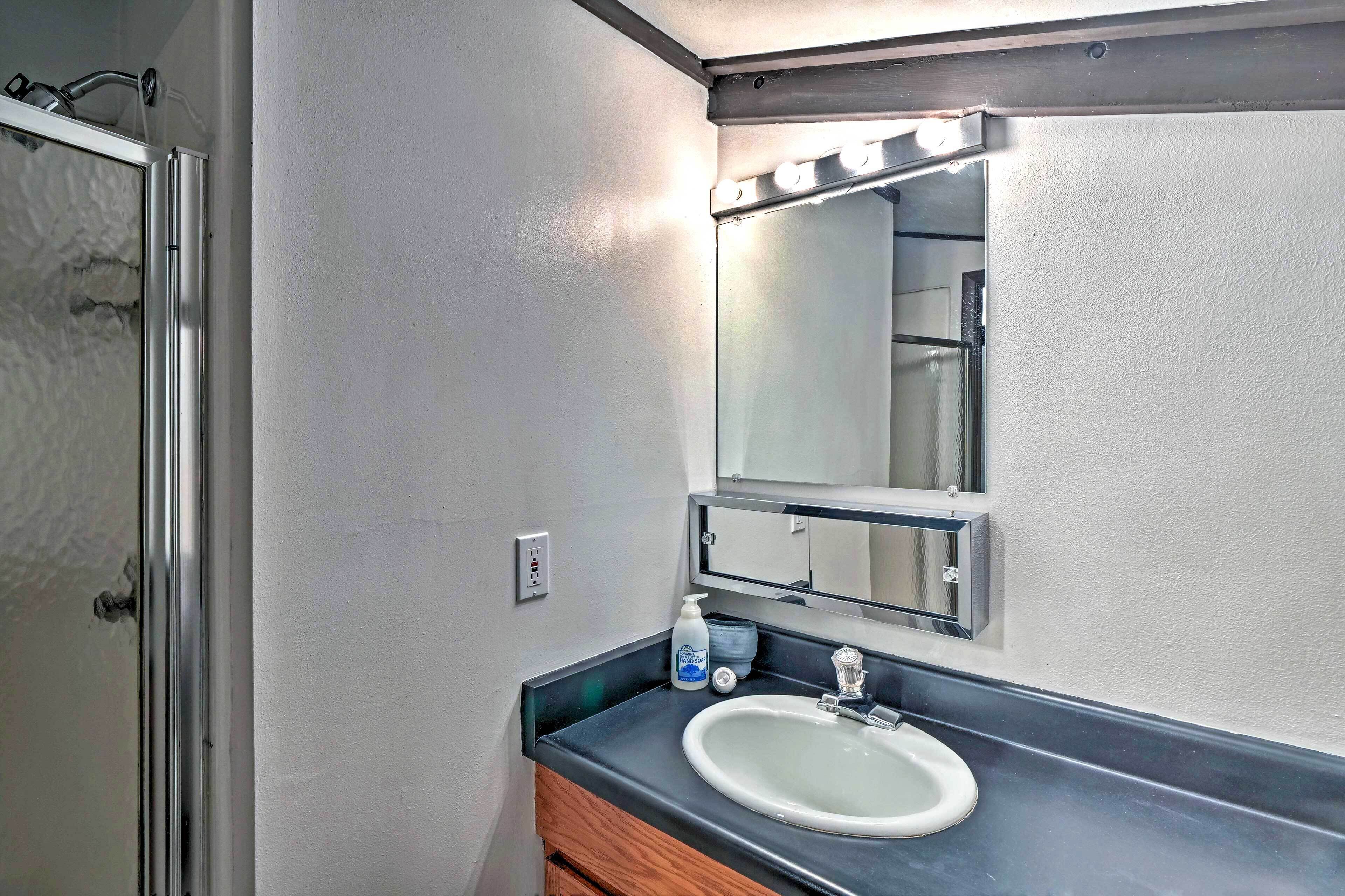 Une salle de bain avec un lavabo blanc, un miroir avec éclairage intégré et une porte de douche.