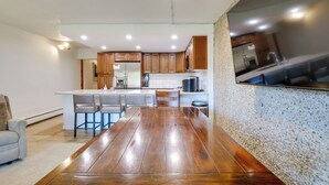A modern kitchen with wooden cabinets, a central island with bar stools, and a dining table. - Beautiful Breck Townhome w/ Pool: 1 Mi to Main St! (Breckenridge)