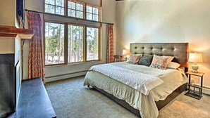 A bedroom with a large bed, a nightstand, a lamp, and a view of trees through large windows. - Beautiful Breck Townhome w/ Pool: 1 Mi to Main St! (Breckenridge)