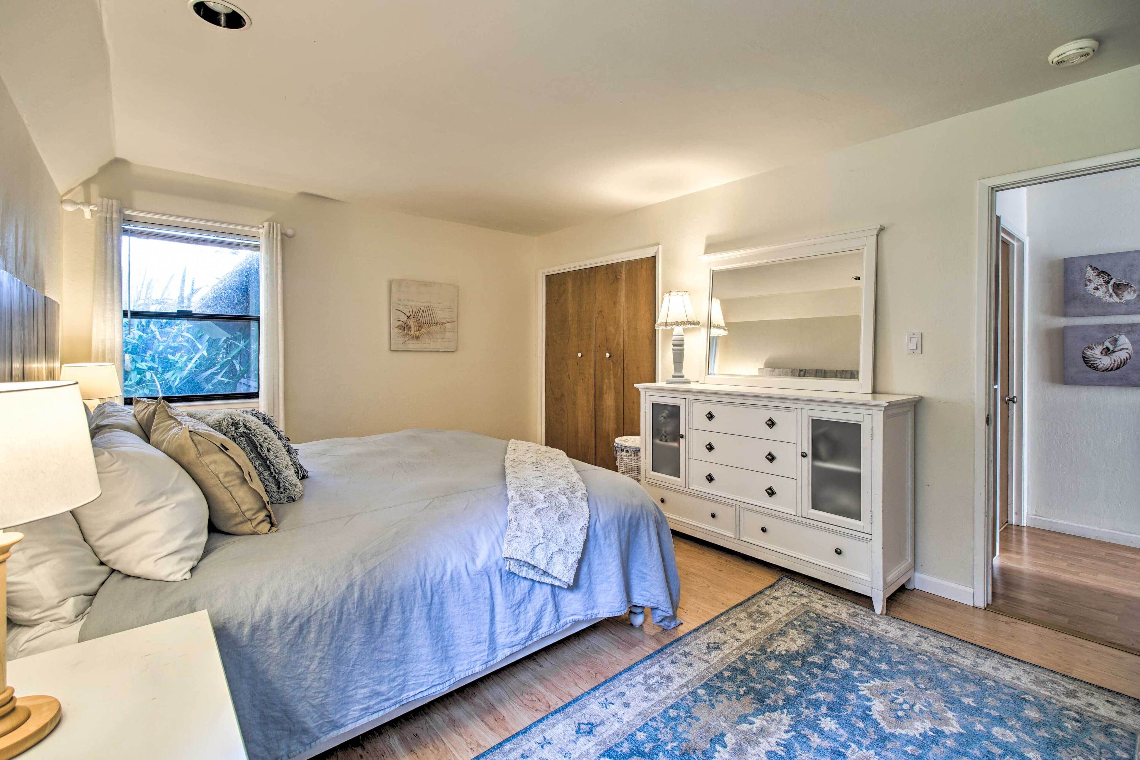 A bedroom with a bed, bedside table, lamp, dresser, and a window with curtains.
