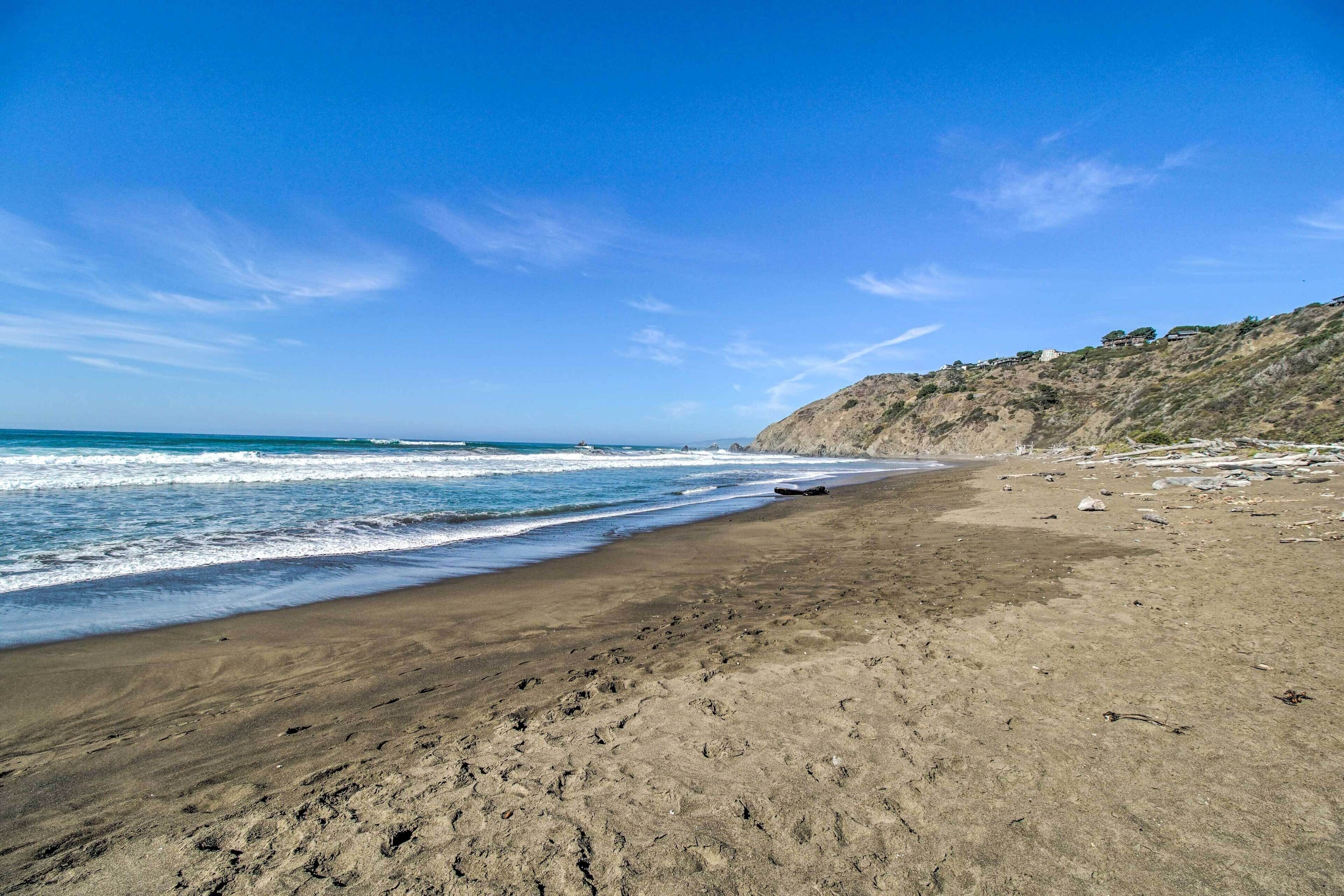 Une plage avec un rivage sablonneux, des vagues et une colline rocheuse en arrière-plan.