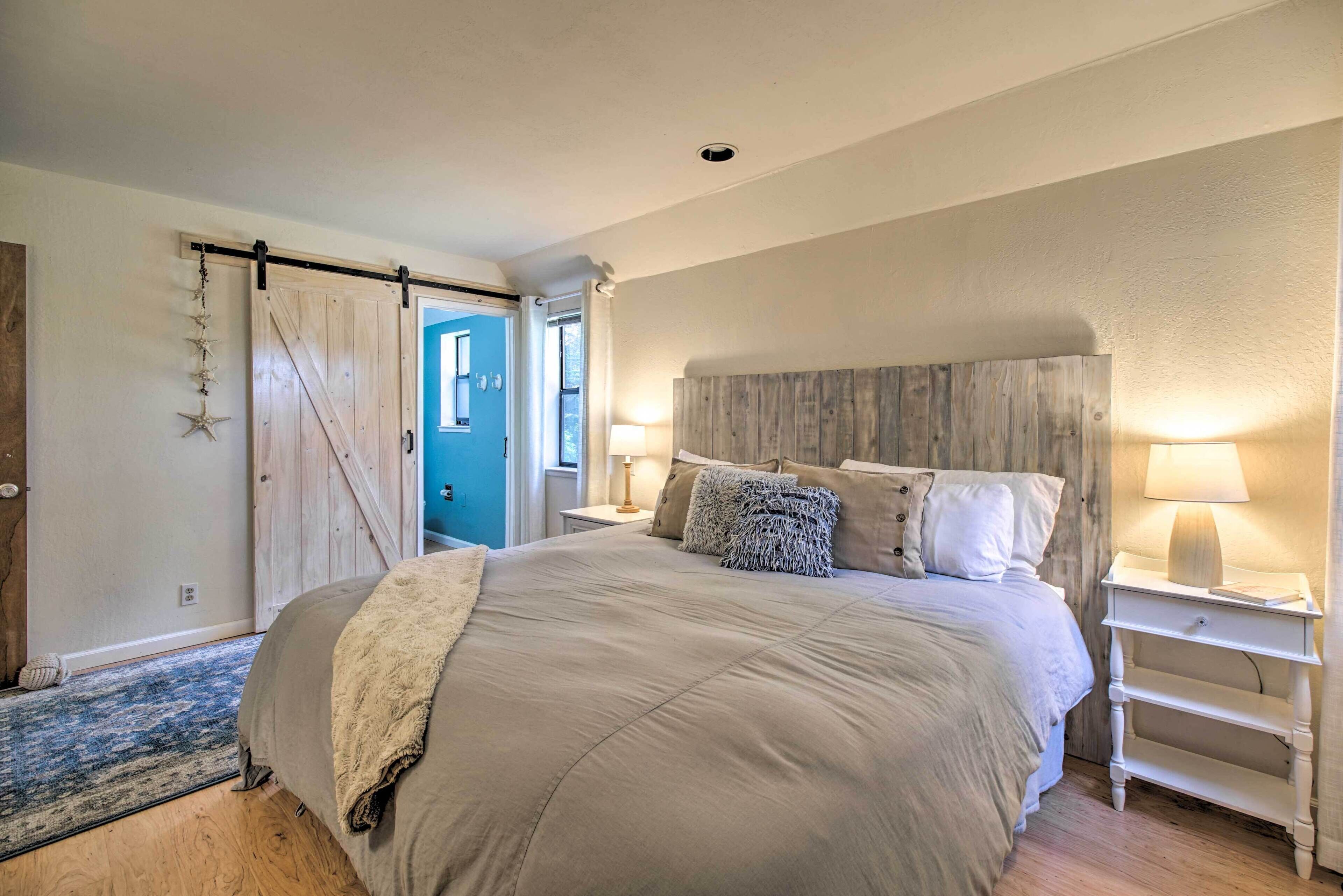 Quarto com uma cama grande, cabeceira de madeira, duas mesas de cabeceira com luminárias, uma porta azul e um enfeite de estrela-do-mar na parede.