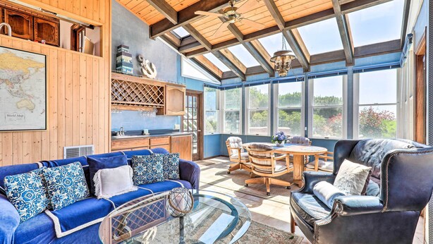 A spacious room with a large wooden ceiling, a glass-enclosed sunroom, a blue sofa, a leather armchair, and a dining table with chairs. - Oceanfront Irish Beach 'sea Haven' Home w/ Hot Tub (Manchester)