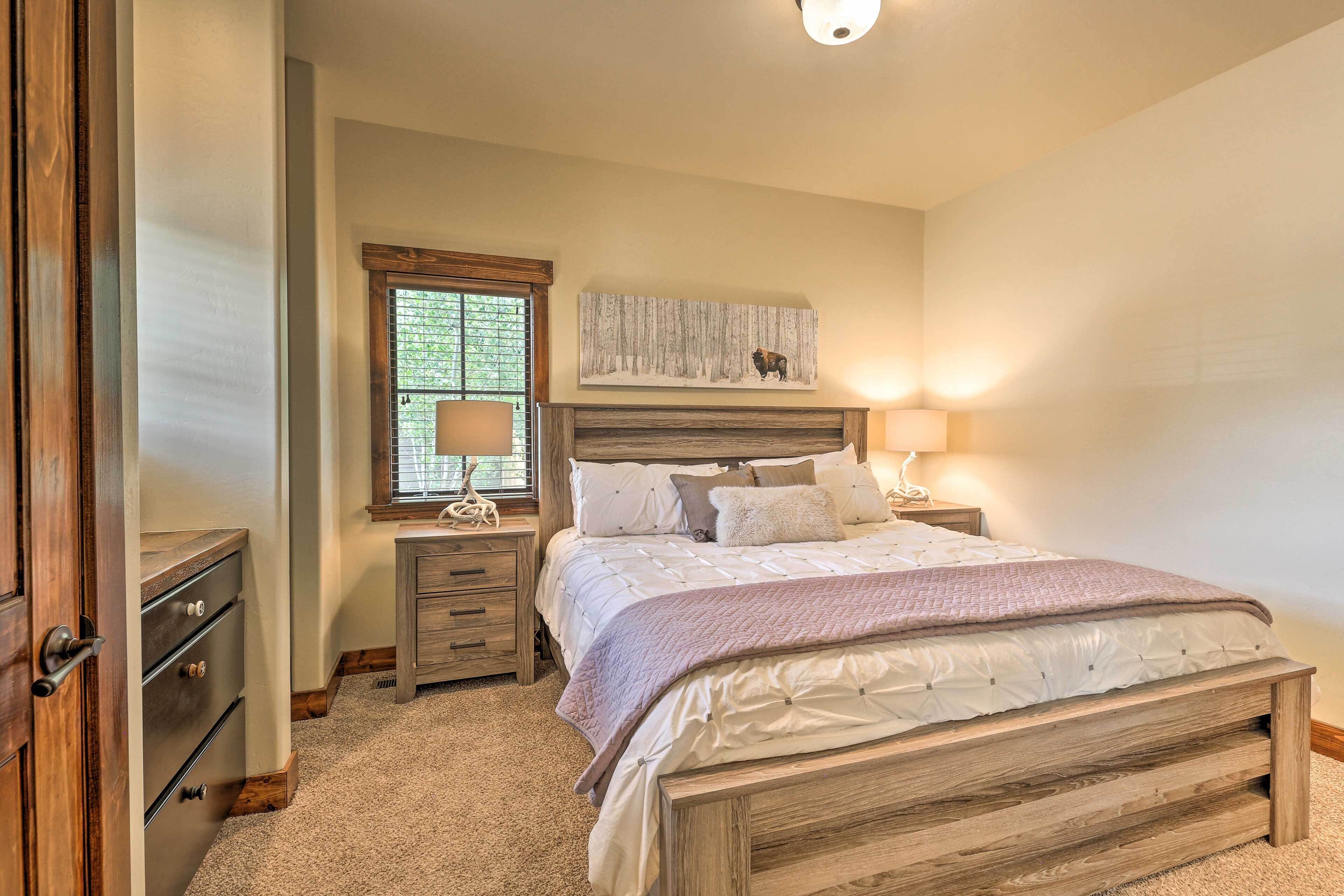 Une chambre à coucher avec un lit en bois, une table de chevet avec une lampe, une commode et une fenêtre avec des stores.