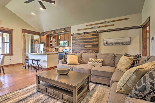 A modern living room with a sofa, coffee table, and a kitchen area in the background. - Walk to Main St & Marina: Grand Lake Cabin! (Grand Lake)