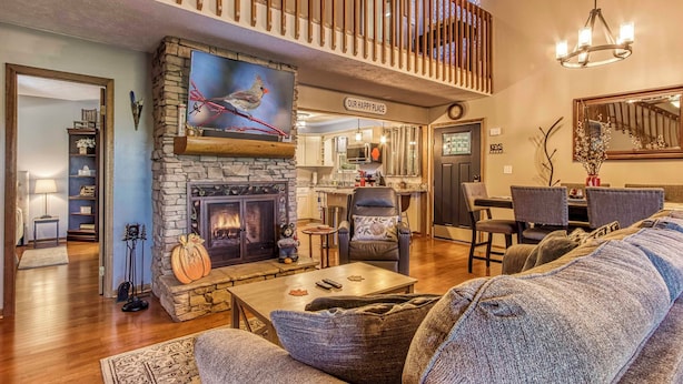 A cozy living room with a stone fireplace, a comfortable sofa, and a dining area in the background. - Cozy Cabin w/ Mountain Views Near Skylift Park! (Gatlinburg)