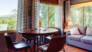 A cozy room with a round wooden table, four chairs, a sofa, and large windows with patterned curtains. - Cozy Cabin w/ Mountain Views Near Skylift Park! (Gatlinburg)