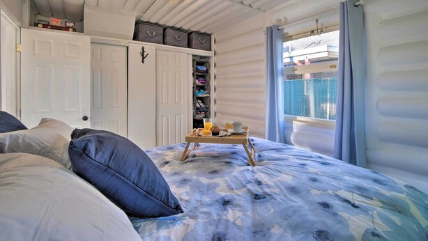 Un dormitorio con cama, armario, una mesita de apoyo con alimentos para el desayuno y una ventana con cortinas.
