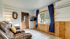 Interior acogedor de una cabaña con sofá de cuero, paredes de madera, un ventanal con cortinas y un televisor montado.