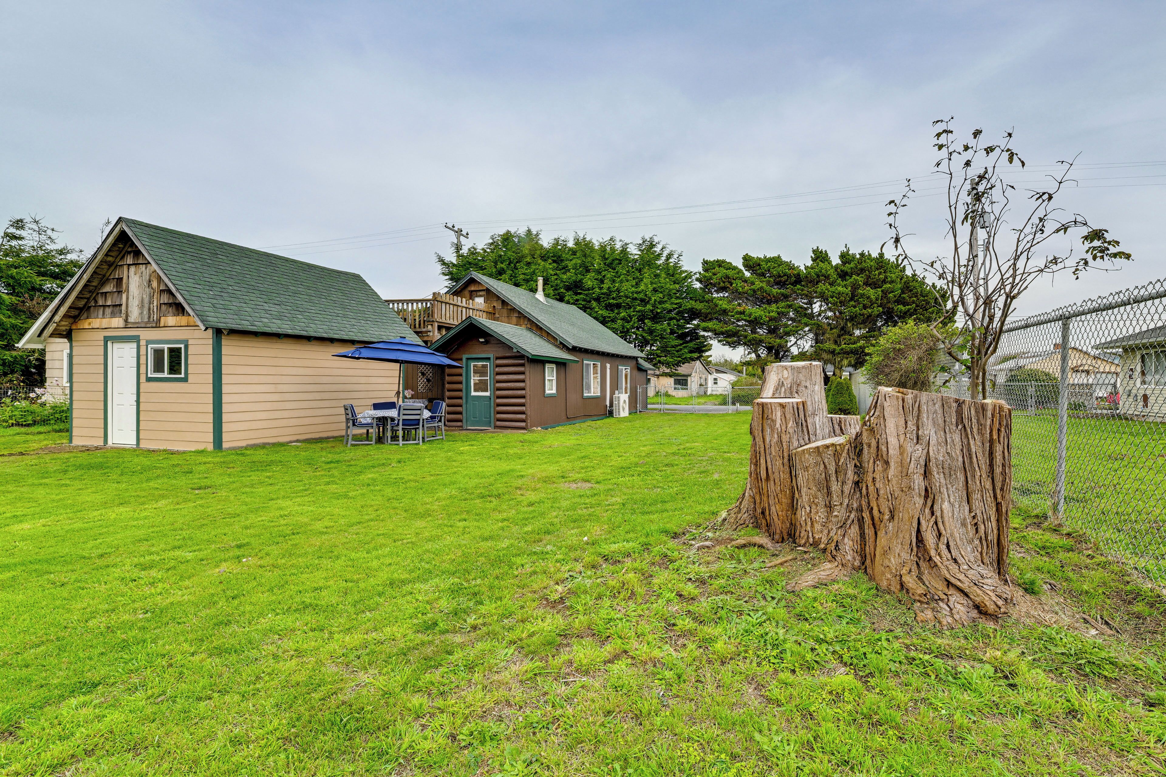 A cabin with a green roof, a small porch, and a dining area with outdoor seating.
