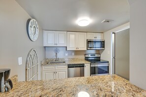 Una cocina con armarios blancos, encimera de granito, refrigerador de acero inoxidable, lavavajillas y microondas.