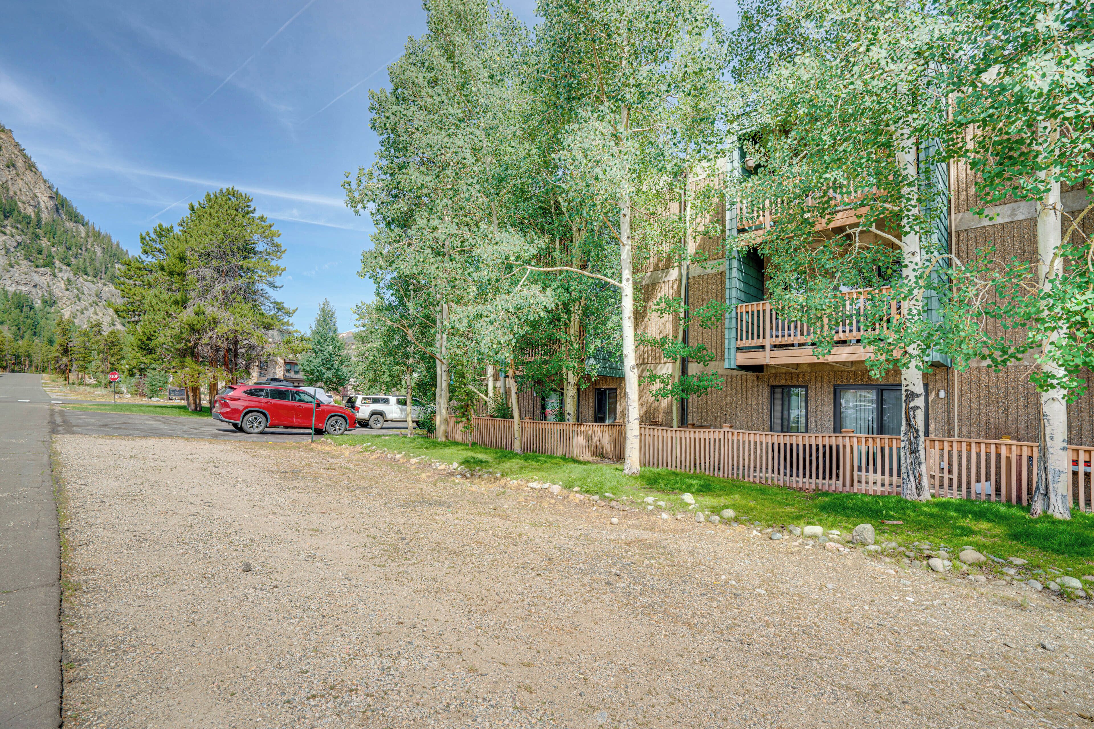 A building with a wooden deck, a gravel driveway, and a red car parked in front.